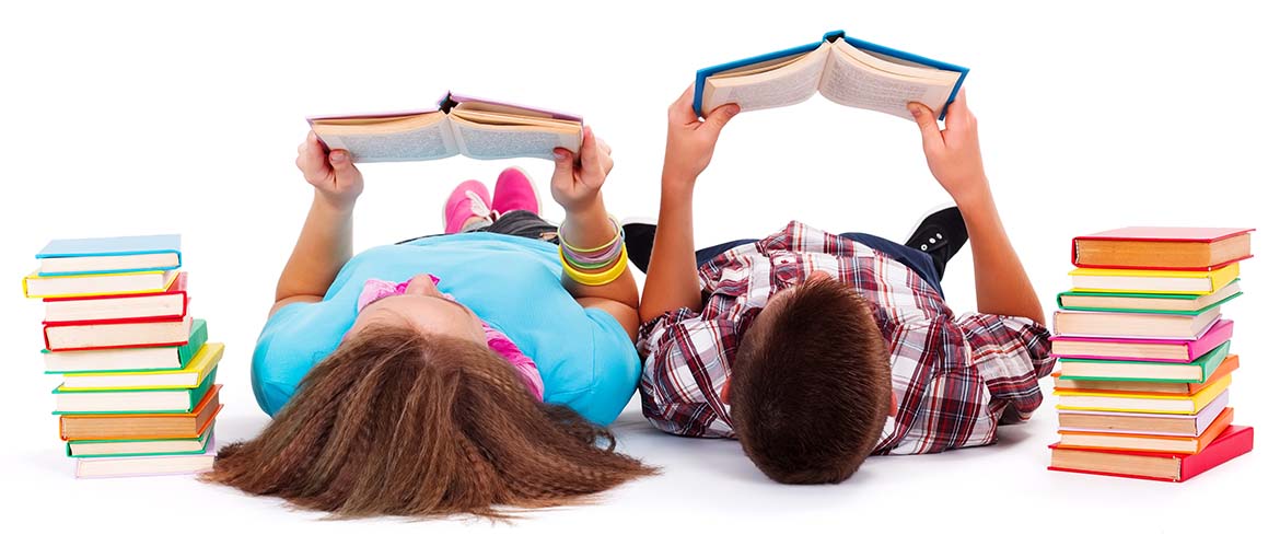 2 elementary students reading while lying down, with a stack of books on either side.