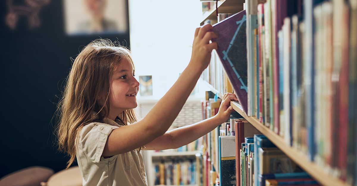 A girl reaches eagerly for a book on a library shelf