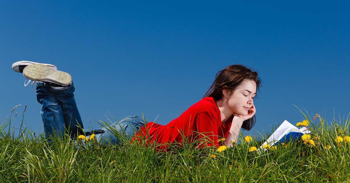 Middle school age teen reading a book in a grassy field.